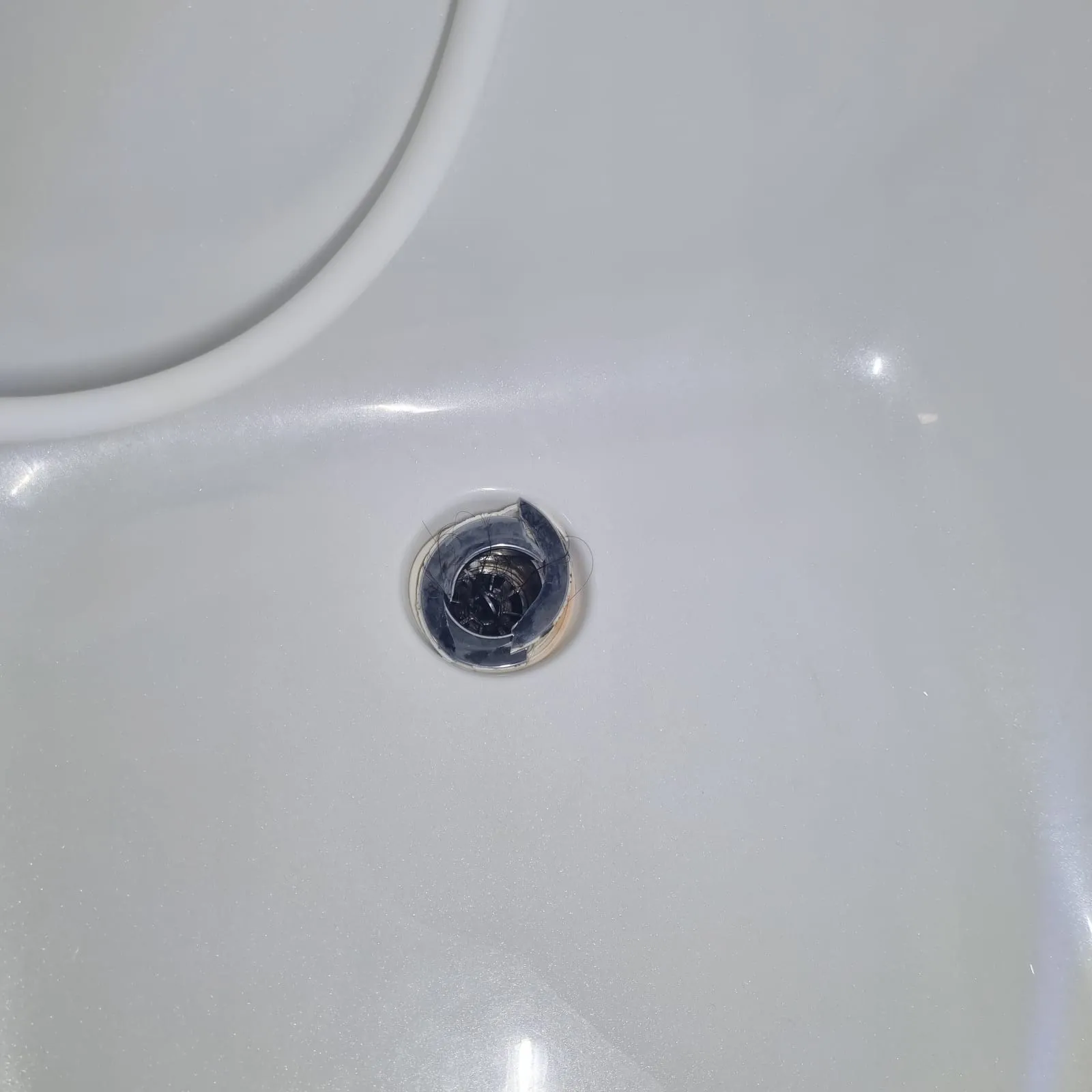 욕조 바닥 배수구의 검은 부품이 여러 조각으로 깨져 있고 머리카락이 걸려 있다